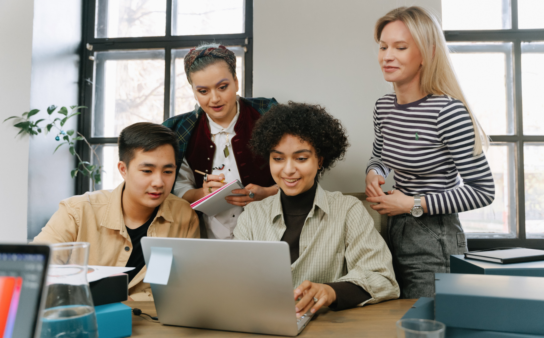 A small group collaborates around a laptop, smiling as they work together